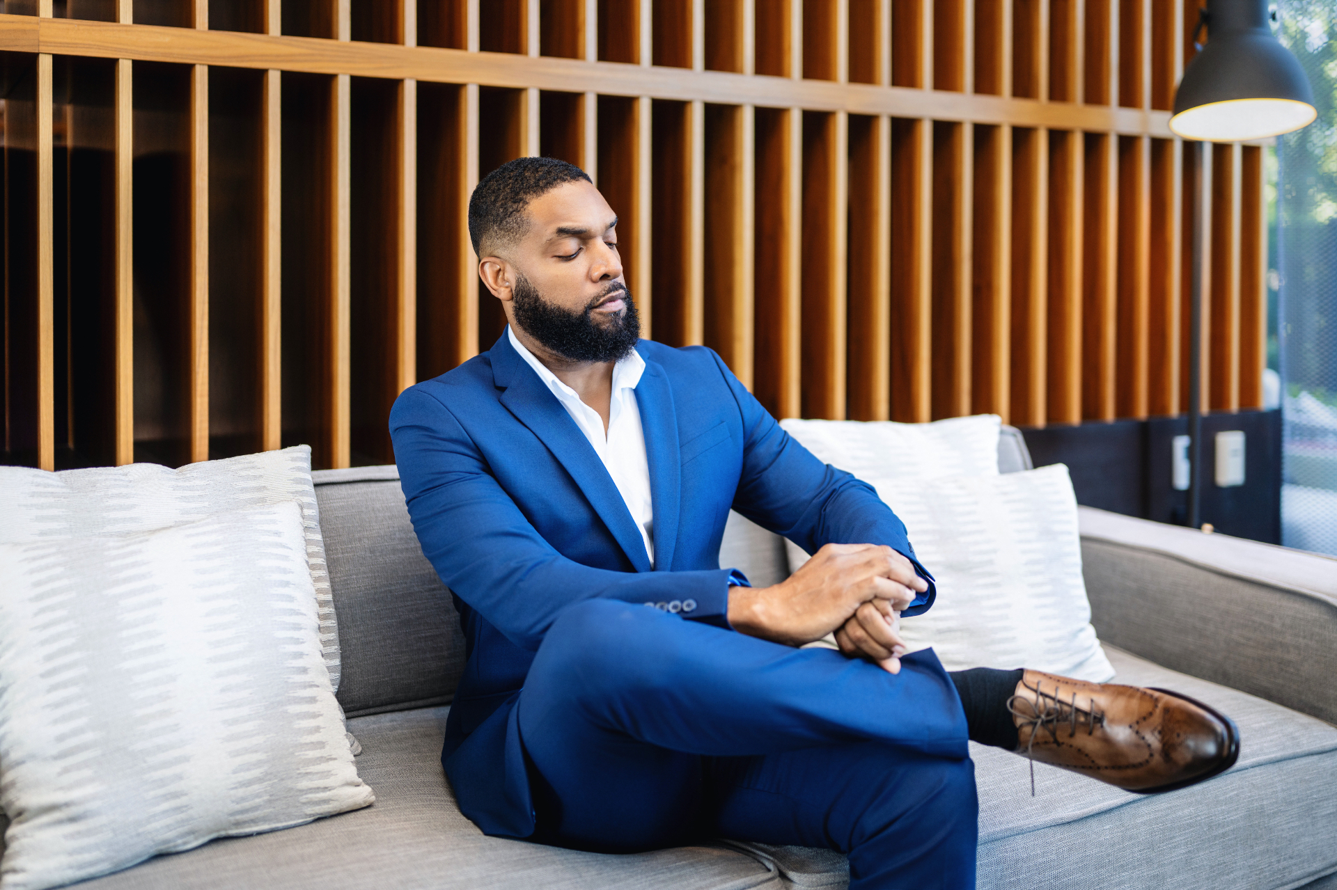 Jay Cameron seated on a sofa in a blue suit, in a moment of reflection